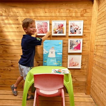 An adorable kid hangs 8x8 prints on a wooden wall.