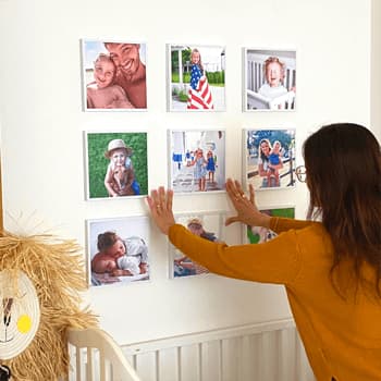 A young mom sticks white photo frames on a baby's room wall.