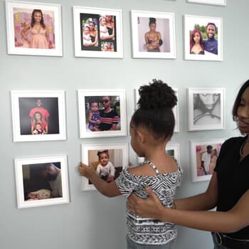 A child hangs white-framed photo tiles on a green wall.